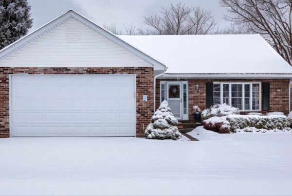 A snow-covered garage beside a house, featuring weather stripping on the garage door and insulated walls for winter protection.