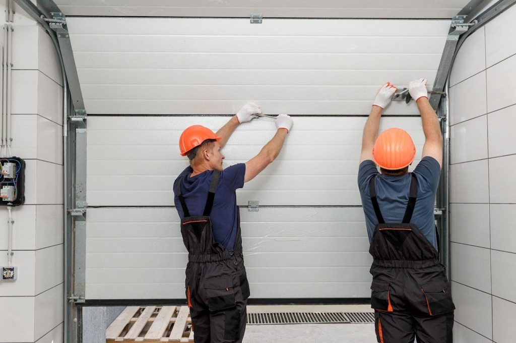 Two men in overalls are fixing a garage door, highlighting their collaboration and skills